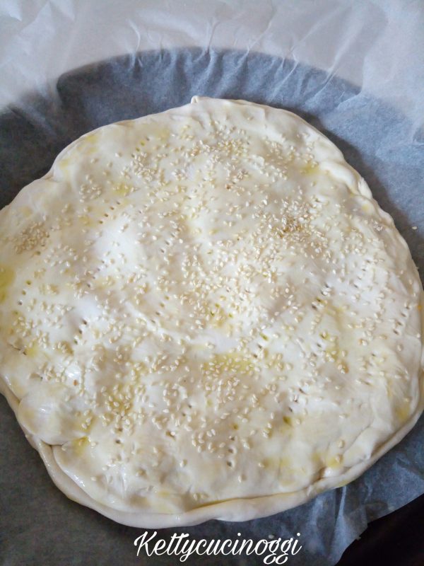 Una volta che abbiamo assemblato la base della <i><b>Parigina torta salata</b></i> copriamo con la pasta sfoglia, pennelliamo con un emulsione di olio evo e acqua e aggiungiamo i semi di sesamo.