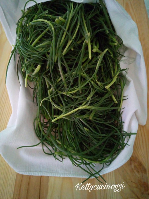 Per preparare gli <i><b>agretti alla mediterranea</b></i>per prima cosa dobbiamo pulire la verdura, eliminiamo con un coltellino la radice alla base, la parte più dura dei gambi e se ci sono le barbette gialle, le laviamo bene sotto l'acqua corrente più volte in modo da eliminare eventuali residui di terra.