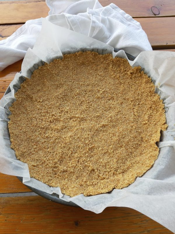 In una teglia da crostata diametro 25, copriamo con la carta a forno, e con il dorso di un cucchiaio compattiamo bene la base.