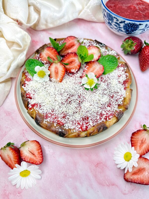 Prima di servire, rimuoviamo delicatamente la cheesecake dalla tortiera e guarniamo con la crema di fragole cocco rapè e fragole fresche.